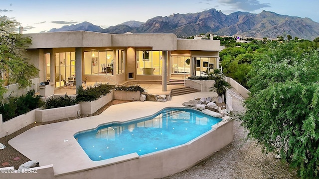 back of property with a fenced in pool, a mountain view, and a patio