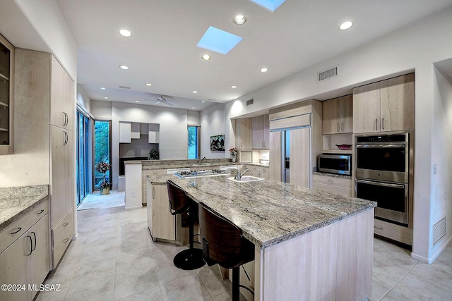 kitchen with light stone countertops, appliances with stainless steel finishes, a skylight, a kitchen breakfast bar, and kitchen peninsula