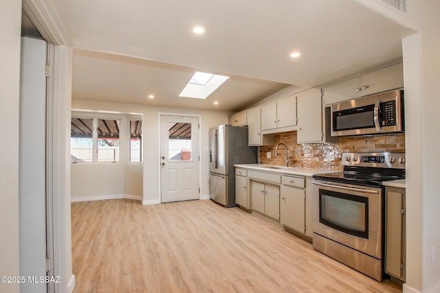 kitchen with tasteful backsplash, sink, light wood-type flooring, appliances with stainless steel finishes, and a skylight