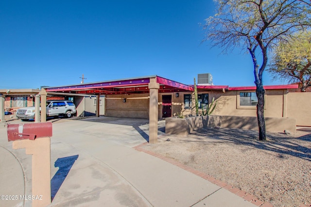 view of front of property with an attached carport, central AC, and stucco siding