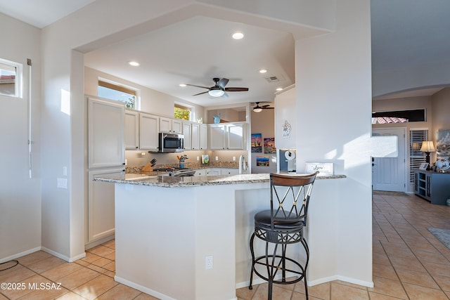 kitchen with white cabinetry, a breakfast bar, light stone counters, and kitchen peninsula