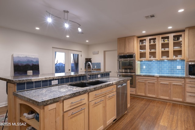 kitchen with sink, a kitchen island with sink, stainless steel appliances, light hardwood / wood-style floors, and light brown cabinetry