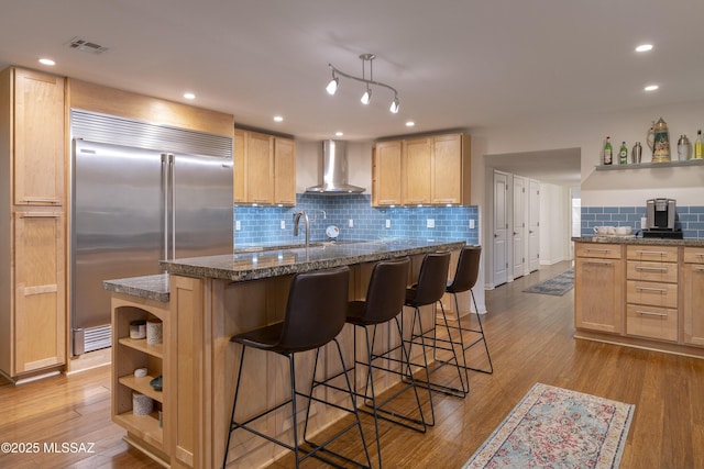 kitchen with built in refrigerator, a center island, light hardwood / wood-style floors, light brown cabinetry, and wall chimney exhaust hood