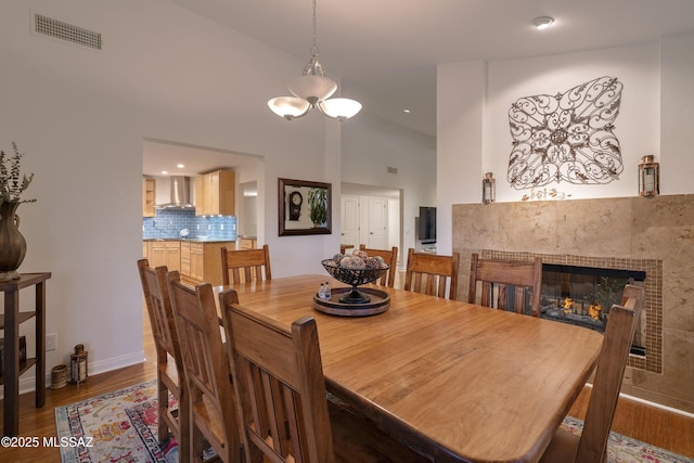 dining space featuring dark hardwood / wood-style flooring, high vaulted ceiling, a tile fireplace, and an inviting chandelier