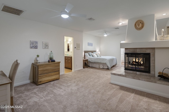 bedroom with ceiling fan, ensuite bath, a fireplace, and light carpet