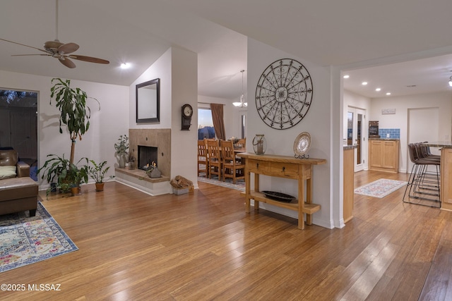 living room with light hardwood / wood-style flooring, vaulted ceiling, ceiling fan, and a multi sided fireplace