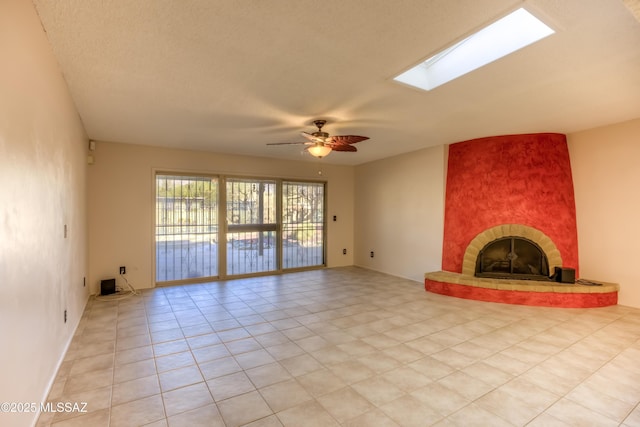 unfurnished living room with ceiling fan, light tile patterned floors, a skylight, and a tiled fireplace