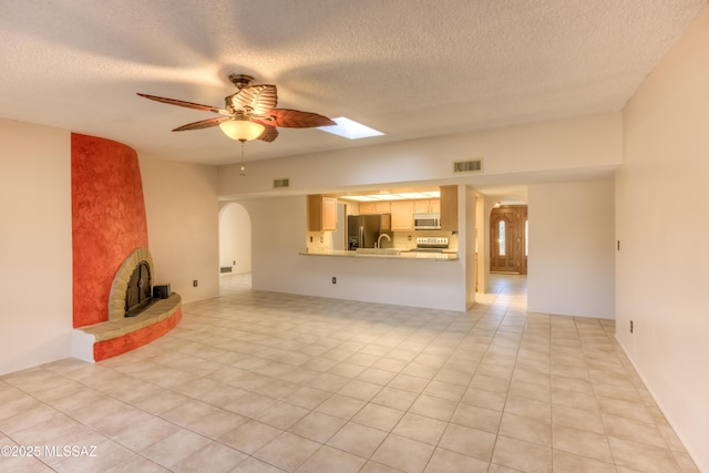 unfurnished living room featuring ceiling fan, light tile patterned flooring, a wood stove, and a textured ceiling