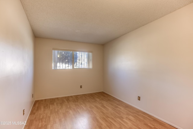 empty room with a textured ceiling and light hardwood / wood-style flooring