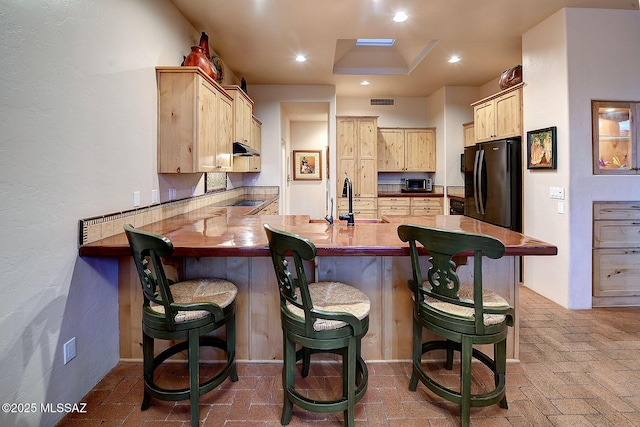 kitchen with a breakfast bar, sink, light brown cabinets, black refrigerator, and kitchen peninsula