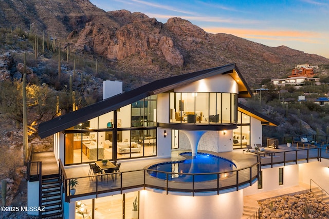 back house at dusk featuring a mountain view, a hot tub, a patio, and a balcony