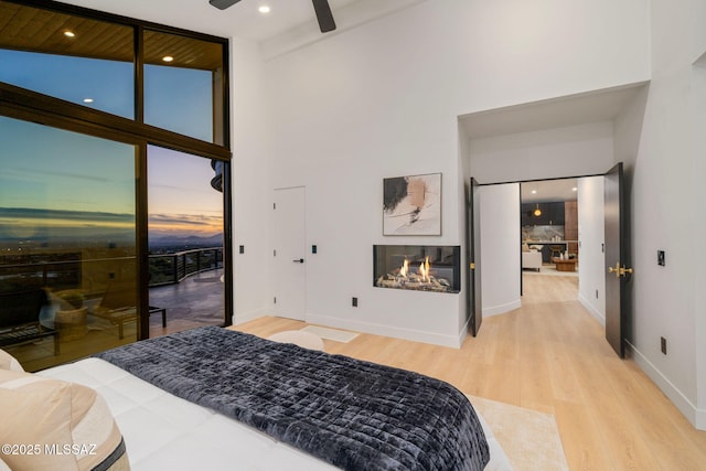 bedroom featuring a multi sided fireplace, a wall of windows, a high ceiling, access to outside, and light hardwood / wood-style flooring