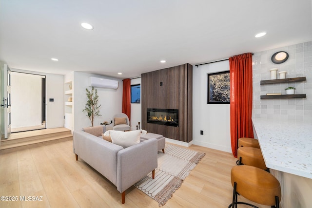 living room with a large fireplace, light hardwood / wood-style floors, and a wall unit AC