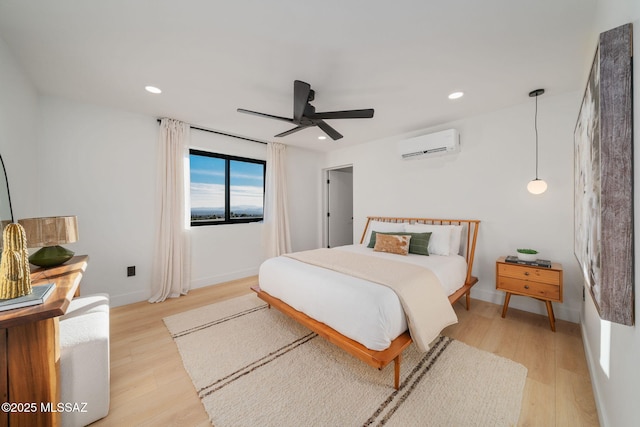 bedroom with a wall mounted air conditioner, light hardwood / wood-style floors, and ceiling fan