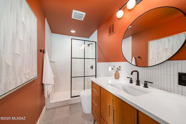 bathroom featuring toilet, a shower with shower door, tile walls, vanity, and tile patterned flooring