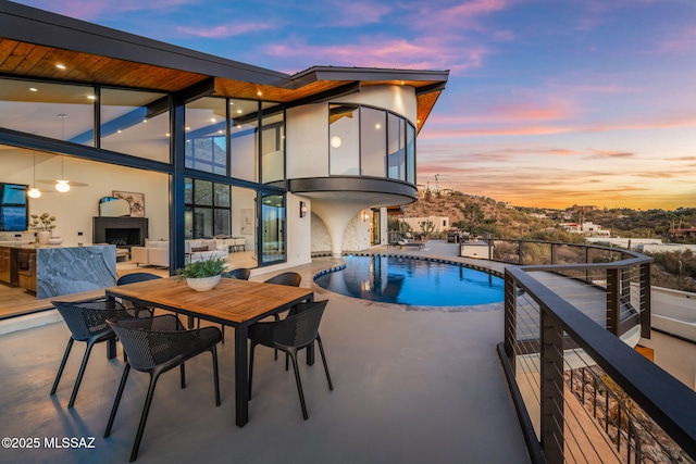 pool at dusk with an outdoor fireplace and a patio area