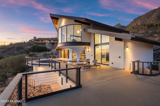 back house at dusk with a balcony, a mountain view, and a patio area