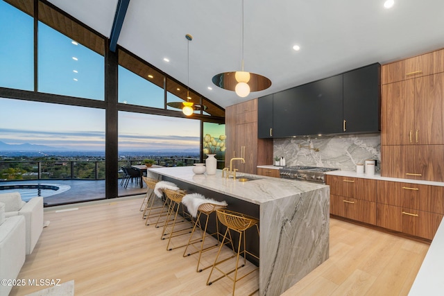 kitchen with sink, a breakfast bar area, hanging light fixtures, expansive windows, and a kitchen island with sink