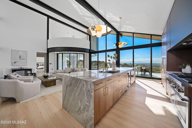 kitchen with floor to ceiling windows, double oven range, an island with sink, light stone countertops, and light hardwood / wood-style floors