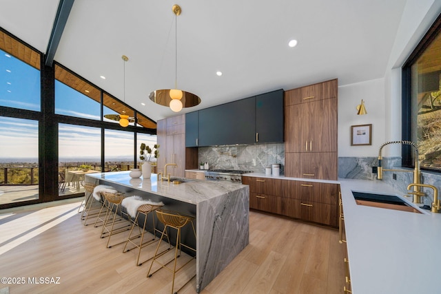 kitchen with floor to ceiling windows, sink, decorative light fixtures, an island with sink, and backsplash