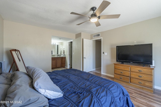bedroom with visible vents, a textured ceiling, ensuite bath, wood finished floors, and baseboards