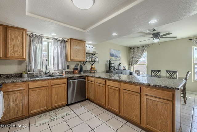 kitchen featuring brown cabinets, a wealth of natural light, stainless steel dishwasher, a sink, and a peninsula