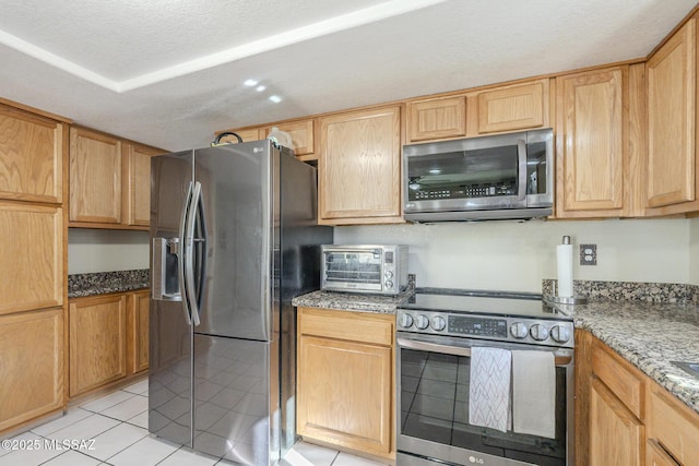 kitchen with light tile patterned floors, a textured ceiling, light stone counters, a toaster, and stainless steel appliances