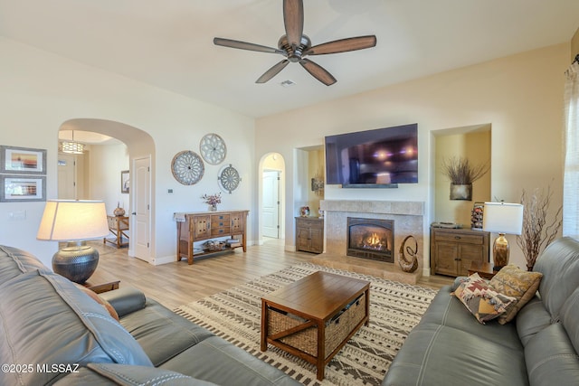 living room featuring a tiled fireplace, ceiling fan, and light wood-type flooring