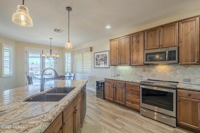 kitchen featuring stainless steel appliances, decorative light fixtures, light stone countertops, and sink