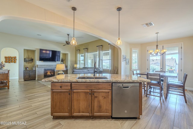 kitchen featuring pendant lighting, dishwasher, sink, a kitchen island with sink, and light stone countertops