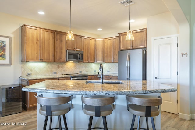 kitchen with sink, light hardwood / wood-style flooring, appliances with stainless steel finishes, a kitchen breakfast bar, and an island with sink