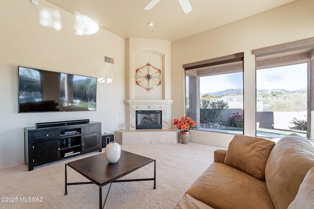 living room featuring a mountain view, light colored carpet, a premium fireplace, and ceiling fan