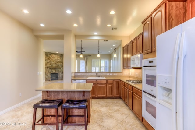 kitchen featuring a kitchen breakfast bar, kitchen peninsula, pendant lighting, sink, and white appliances