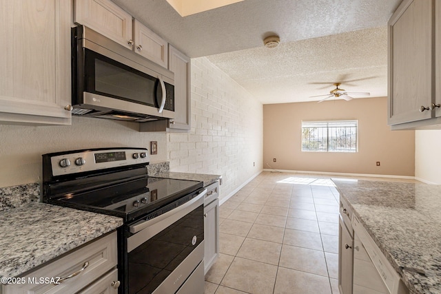 kitchen with stainless steel appliances, a textured ceiling, light tile patterned floors, ceiling fan, and light stone counters