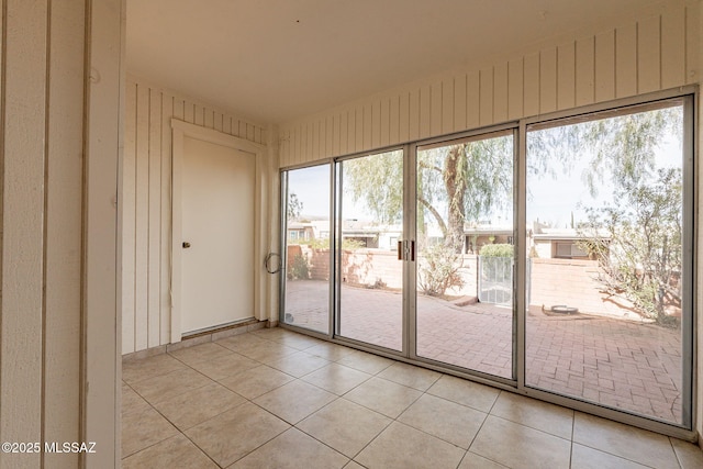 doorway to outside featuring a wealth of natural light, light tile patterned floors, and wood walls