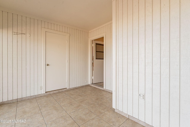 tiled empty room featuring wood walls and ornamental molding