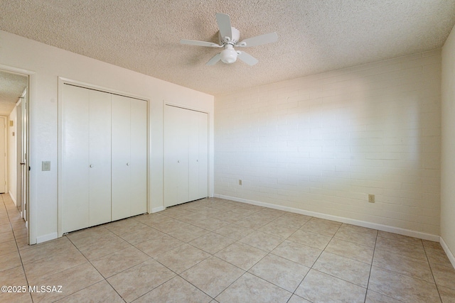 unfurnished bedroom featuring multiple closets, a textured ceiling, brick wall, and ceiling fan