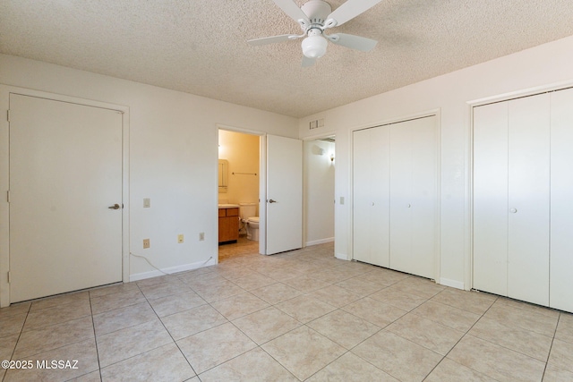 unfurnished bedroom featuring ceiling fan, ensuite bathroom, light tile patterned floors, a textured ceiling, and two closets