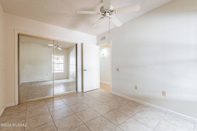 unfurnished bedroom with light tile patterned flooring, a textured ceiling, a closet, and ceiling fan