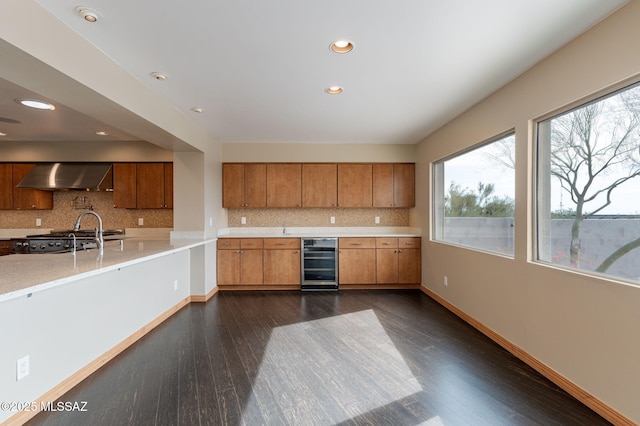 kitchen with dark wood-type flooring, wall chimney range hood, beverage cooler, and backsplash