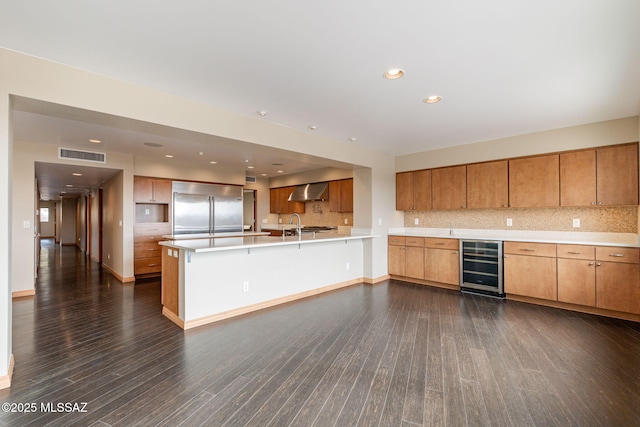 kitchen with wall chimney exhaust hood, built in refrigerator, dark hardwood / wood-style flooring, kitchen peninsula, and beverage cooler