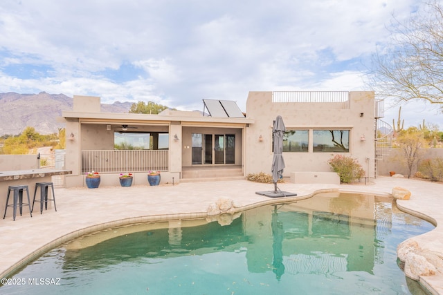 rear view of house with exterior bar, a mountain view, a patio, and solar panels