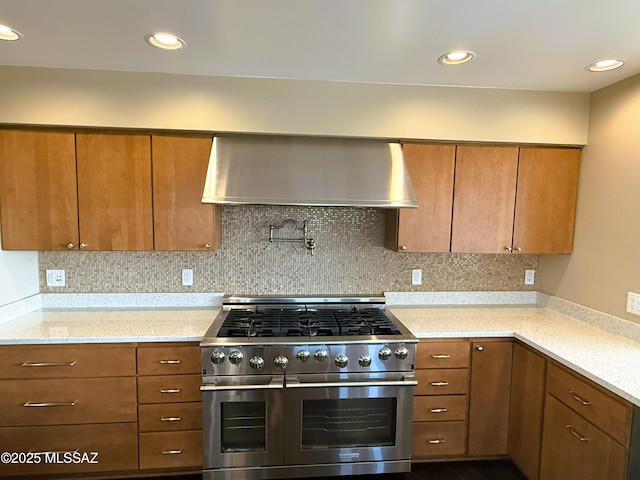 kitchen with tasteful backsplash, double oven range, ventilation hood, and light stone countertops