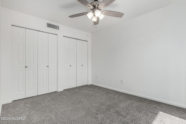 unfurnished bedroom with two closets, ceiling fan, and carpet