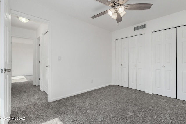 unfurnished bedroom featuring dark colored carpet, two closets, and ceiling fan