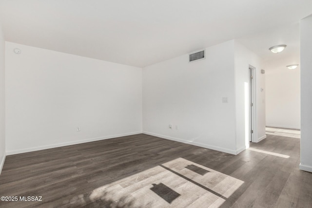 spare room with visible vents, baseboards, and dark wood finished floors