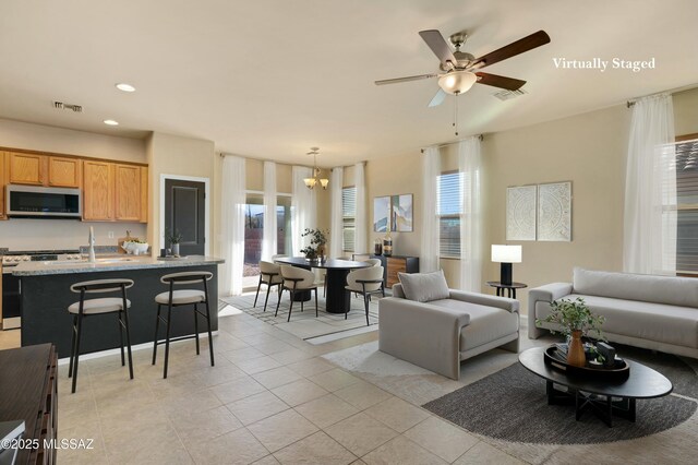 kitchen with ceiling fan, stainless steel appliances, a kitchen island with sink, light stone counters, and sink