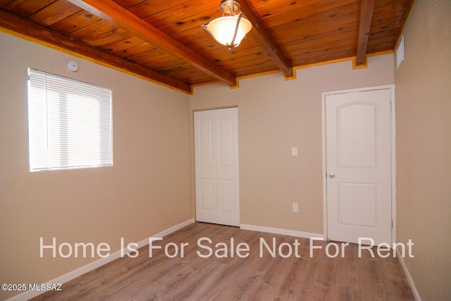 unfurnished bedroom featuring a closet, beamed ceiling, hardwood / wood-style flooring, and wooden ceiling