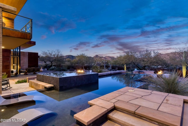 pool at dusk with a mountain view, a fire pit, a patio, and a jacuzzi