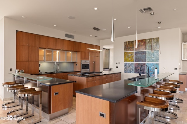 kitchen featuring a large island with sink, appliances with stainless steel finishes, sink, and pendant lighting